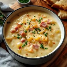 a bowl of soup with ham and cheese in it on a cutting board next to bread