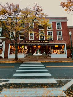 an intersection in front of a store with autumn leaves on the ground and trees lining the street