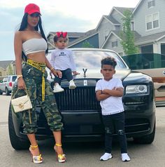 a woman and two children standing in front of a car