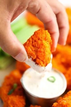 a person dipping something into a small bowl with ranch dressing on it and carrots in the background