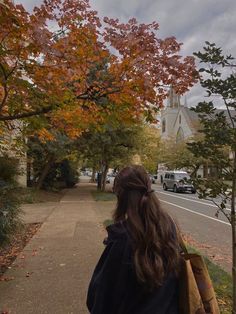 a woman is walking down the sidewalk in front of some trees with orange and red leaves