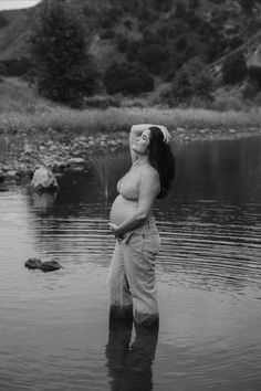 a pregnant woman standing in the water with her belly wrapped around her waist, looking up into the sky