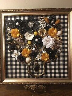 an ornate gold frame with buttons and flowers in it on top of a wooden table