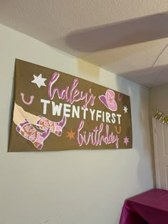 a birthday sign hanging on the wall above a table with a purple cloth draped over it