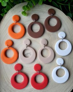 six pairs of earrings sitting on top of a piece of wood next to green leaves