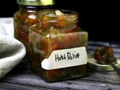 two jars filled with pickles sitting on top of a table next to a spoon