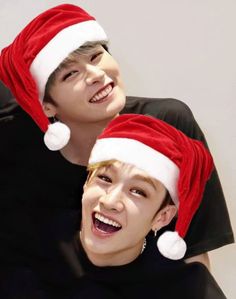 two young men wearing christmas hats and smiling at the camera with one man's face to his chest