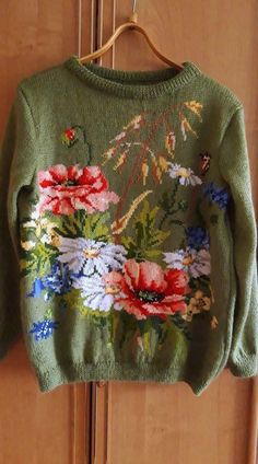 a green sweater with flowers is hanging on a door