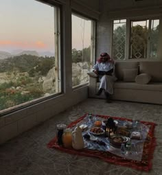 a man sitting on a couch in front of a window with food and drinks on it