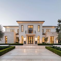 a large white house with lots of windows and bushes in front of the entrance to it