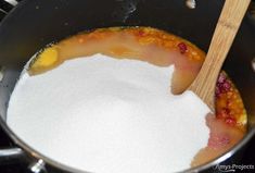 a pan filled with sugar and fruit on top of a stove next to a wooden spoon