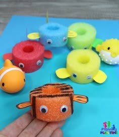 a hand holding a toy with different colored fish on it and other toys in the background