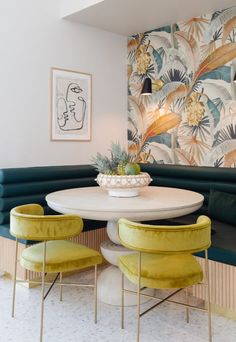 a dining room with green velvet chairs and a white table in front of a floral wallpaper