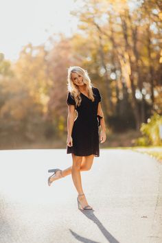 a woman in a black dress is walking down the street with her hand on her hip