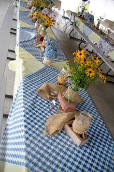 the table is set with blue and white gingham cloths, vases filled with flowers