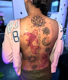 the back of a woman's body with fish and lotus tattoos on her upper back