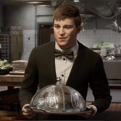 a young man in a tuxedo holding a silver platter with an ornate design on it