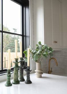 candles are lined up on the kitchen counter next to a vase with greenery in it