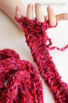 a child's hand holding onto a red crocheted scarf on top of a white table