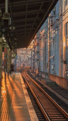 an empty train station with the sun shining down on it's tracks and buildings in the background