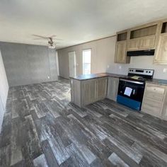 an empty kitchen and living room with wood flooring on the walls, ceiling fan in the corner