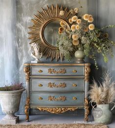 an ornate dresser with flowers on top and a mirror in the corner next to it