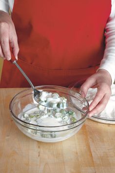 a person in an apron is mixing something in a bowl with a spoon on a wooden table