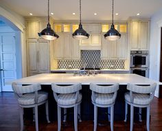 a large kitchen island with four stools in front of it and lights hanging from the ceiling