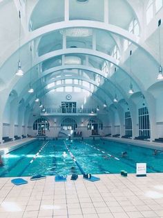 an indoor swimming pool with people in the water and lights hanging from the ceiling above