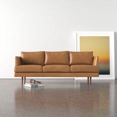 a brown leather couch sitting on top of a hard wood floor next to a white wall