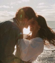 a man and woman kissing in front of the ocean with sun shining through their hair