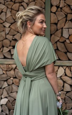 a woman in a green dress standing next to stacks of logs and holding a bouquet