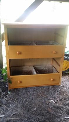 an old dresser is sitting outside on the ground next to some grass and dirt with plants growing in it