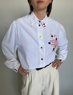 "Vintage White Blouse with Colourful Embroidery and Buttons | White Viscose Shirt for Women Size M - L, with beautiful details. Composition: 100% viscose. In beautiful vintage condition. Measurement of the vintage white blouse lying flat: Chest: 54 cm | 21.3\" Length: 70 cm | 27.6\" Sleeves: 68 cm | 26.8\" Shoulders: 42 cm | 16.5\" The model wearing the white embroidered blouse is size S, 1,68 m | 5.5 feet tall; chest: 88 cm | 35\", waist: 68 cm | 26\", hips: 88 cm | 35\". Whiteaporter is dedica Vintage White Blouse, Colourful Embroidery, White Embroidered Blouse, Tall Chest, Chic Blouses, Pleated Pants, Shirt For Women, White Shirts, Flat Chest