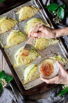 someone using a spatula to stir cabbage on a baking sheet with seasoning in a bowl