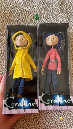 two action figures in plastic packaging on carpeted area with hand holding the same item