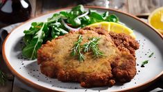 two fried meat patties on a plate with greens and lemon wedges