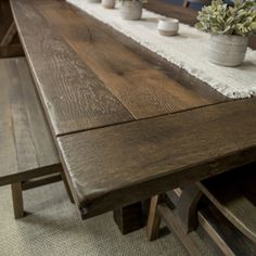 a long wooden table with two planters on each side and one bench at the end