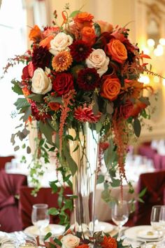 a tall vase filled with red and orange flowers on top of a table covered in silverware