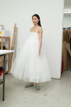 a woman standing in front of a white wall wearing a dress with straps on it