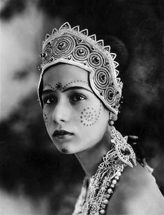 an old black and white photo of a woman with face paint on her face, wearing a headdress