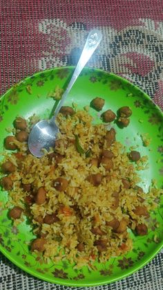 a green plate filled with rice and meat on top of a red table cloth next to a silver spoon