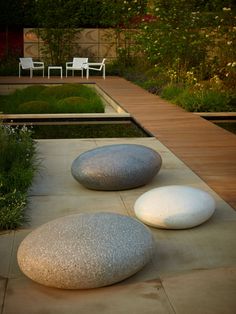 two large rocks sitting on top of a cement slab next to a garden area with white chairs