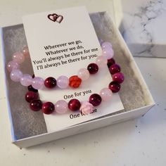 two bracelets with pink and red beads in a white box on a marble table