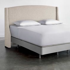 an upholstered bed with white pillows and linens on the headboard is shown