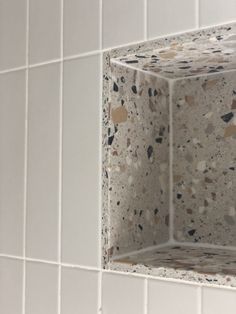 a white tiled wall with a square shaped object in the middle and small speckles on it