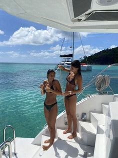 two women in bikinis standing on the bow of a boat