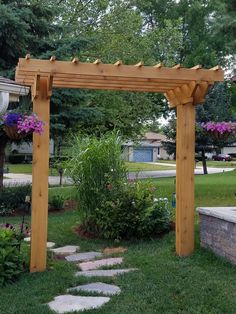 a wooden pergoline in the middle of a yard with flowers and plants around it