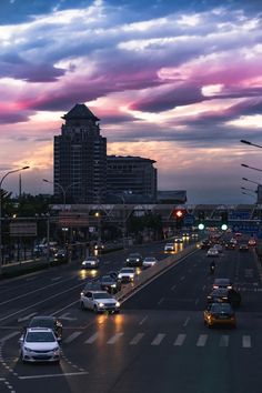 cars driving down the road at dusk with city buildings in the background