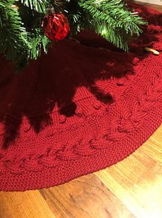 a red knitted christmas tree skirt on the floor next to a small fir tree